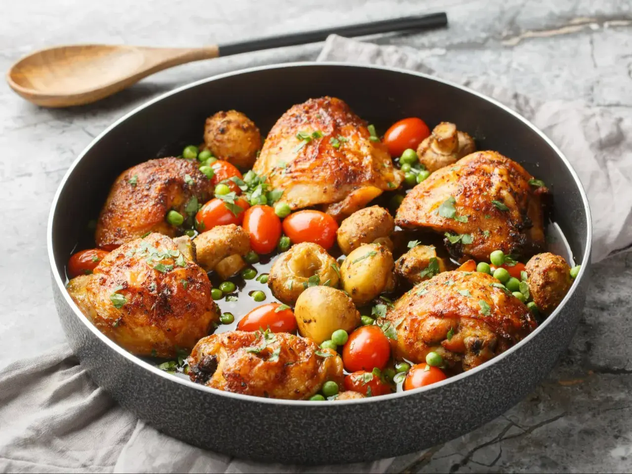 Soczyste udka kurczaka pieczone z ziemniakami, pomidorkami i groszkiem w patelni.